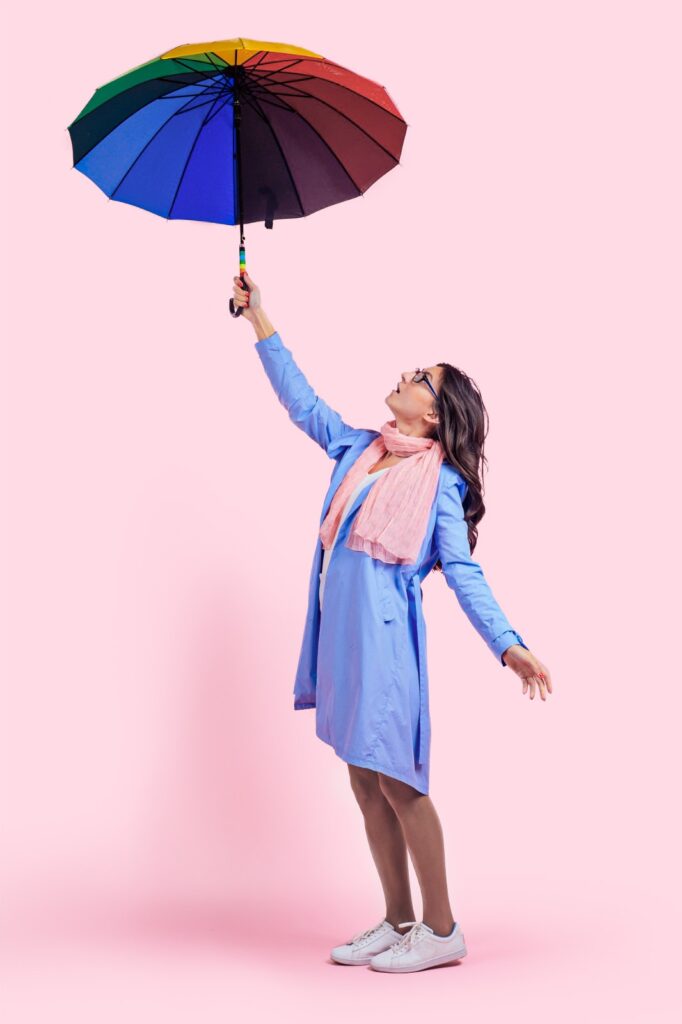 Frau vor rosa Hintergrund mit buntem Regenschirm